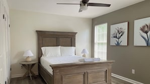 Ein Schlafzimmer mit einem hölzernen Bett, zwei Nachttischen mit Lampen, einem Deckenventilator und zwei floralen Wandbildern.