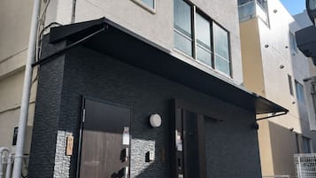 Un bâtiment moderne doté d’un toit plat, d’une enseigne en bois ornée de caractères japonais et d’une porte équipée d’un clavier pour l’ouverture à code.