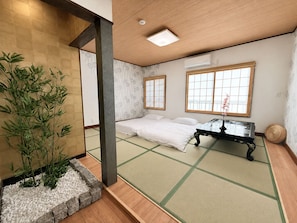 A traditional Japanese room with tatami flooring, a bed, a table, and a bamboo plant.