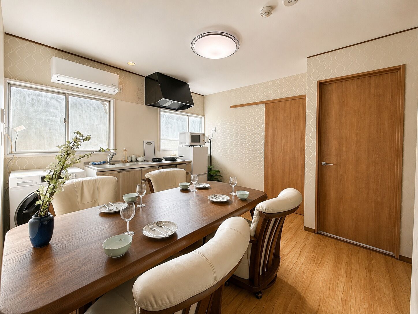 A modern kitchen with a dining area, including a wooden table set for four, a built-in oven, and a microwave.