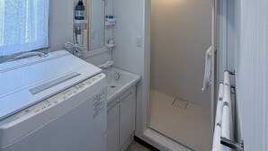 Un baño moderno con lavadora integrada, cabina de ducha de vidrio y una pila de toallas en un perchero.
