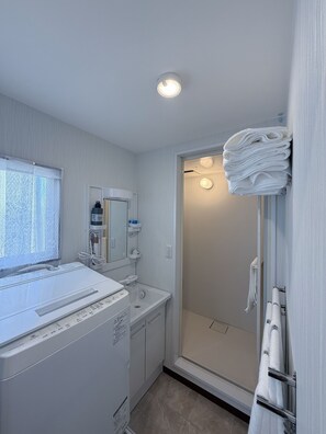Ein modernes Badezimmer mit eingebauter Waschmaschine, einer Duschkabine aus Glas und einem Stapel Handtücher auf einem Ablagegestell.