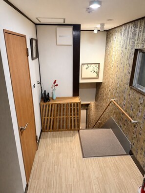 A hotel room with a wooden door, a small desk with a vase, a framed picture, and a staircase with a patterned wall.