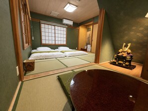 Una habitación japonesa tradicional con suelo de tatami, futón, biombos shoji y un cofre decorativo.