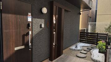 A modern entrance with a wooden door, a keypad, and a small outdoor seating area with steps and a garden.