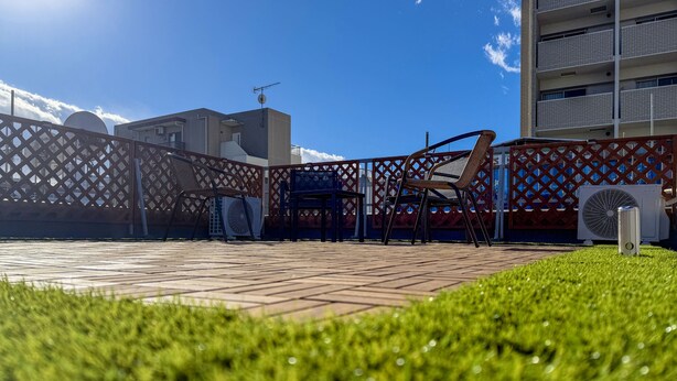 Un patio en la azotea con zona de estar, un ventilador grande y vistas a un edificio de gran altura.