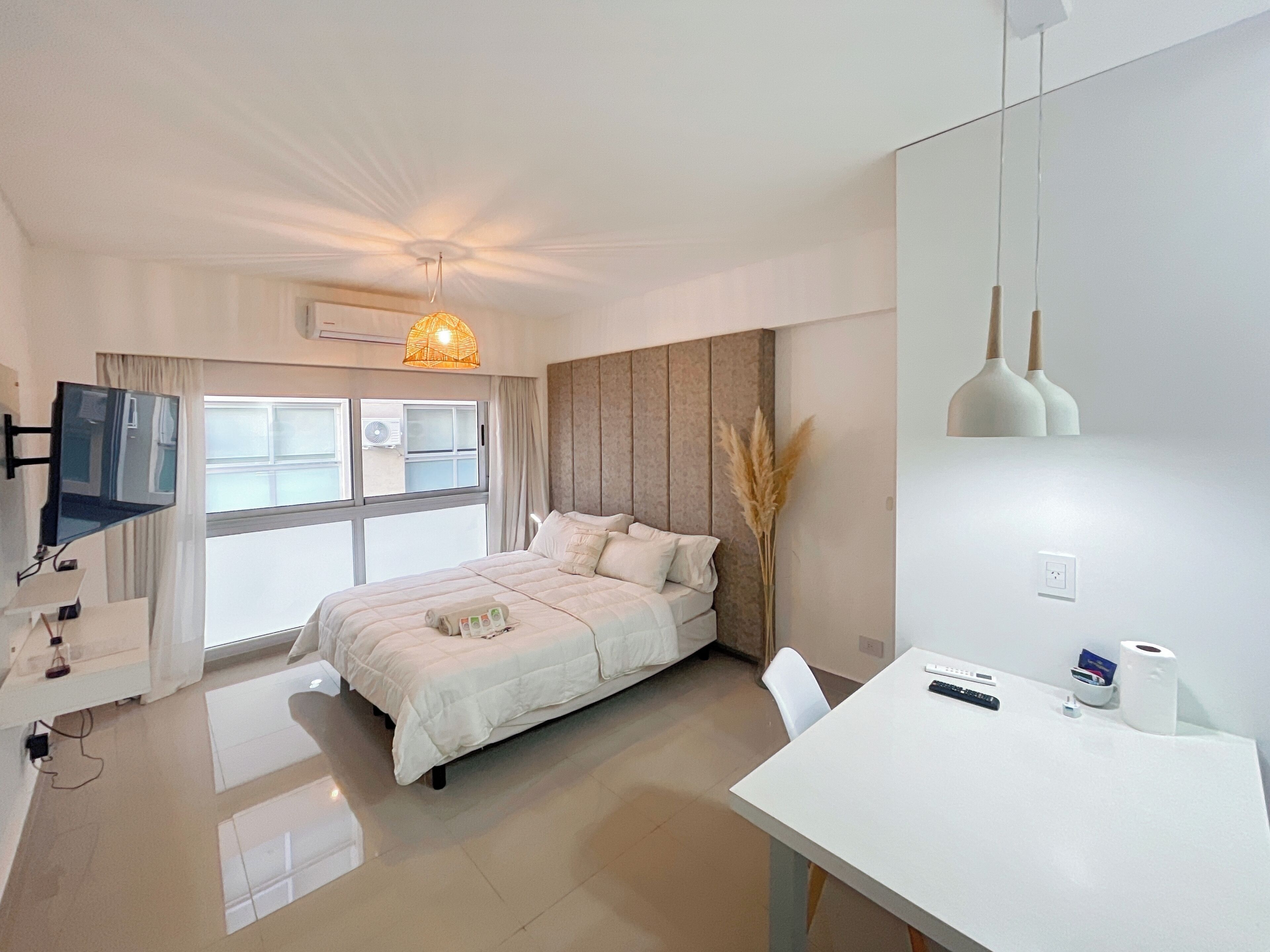 A modern hotel room with a bed, a desk, a TV, and a window with curtains.
