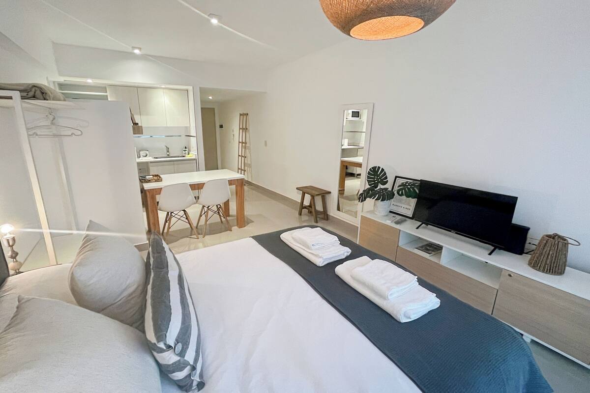 A modern hotel room with a large bed, a TV, a desk, and a kitchenette.