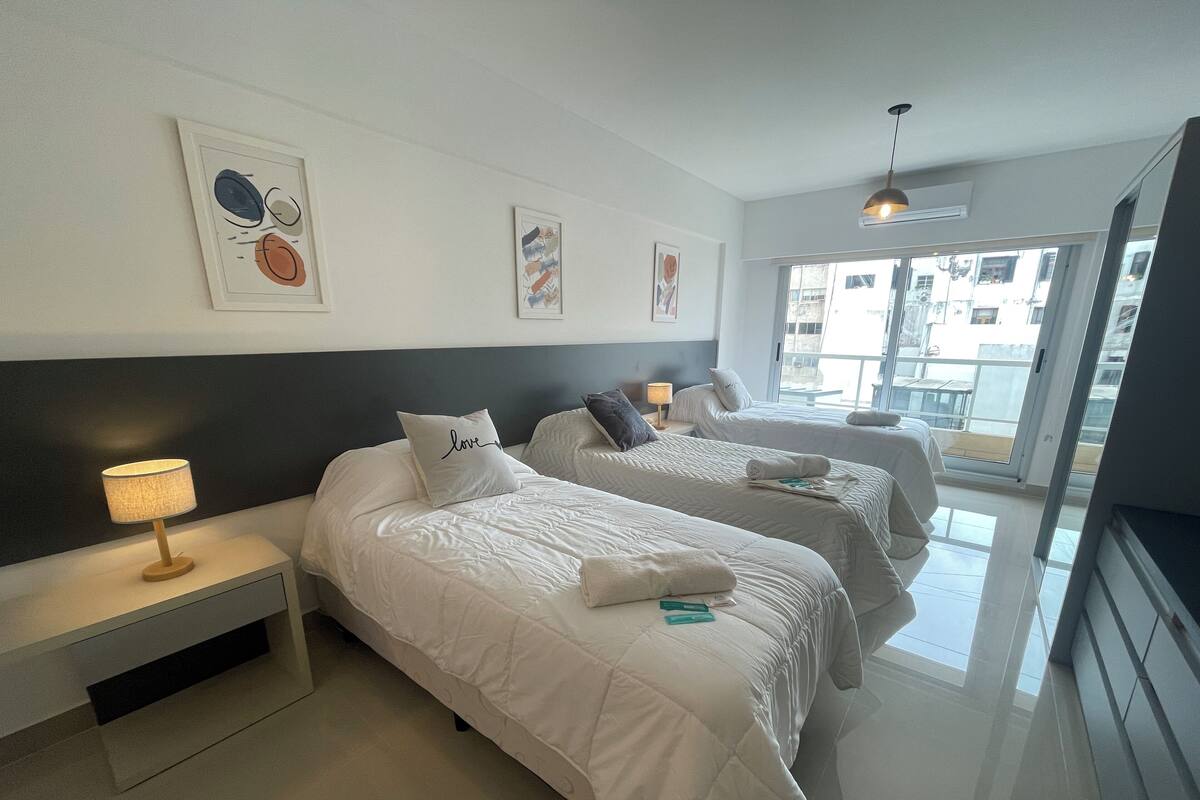 A hotel room with two beds, a bedside table with a lamp, and artwork on the wall.