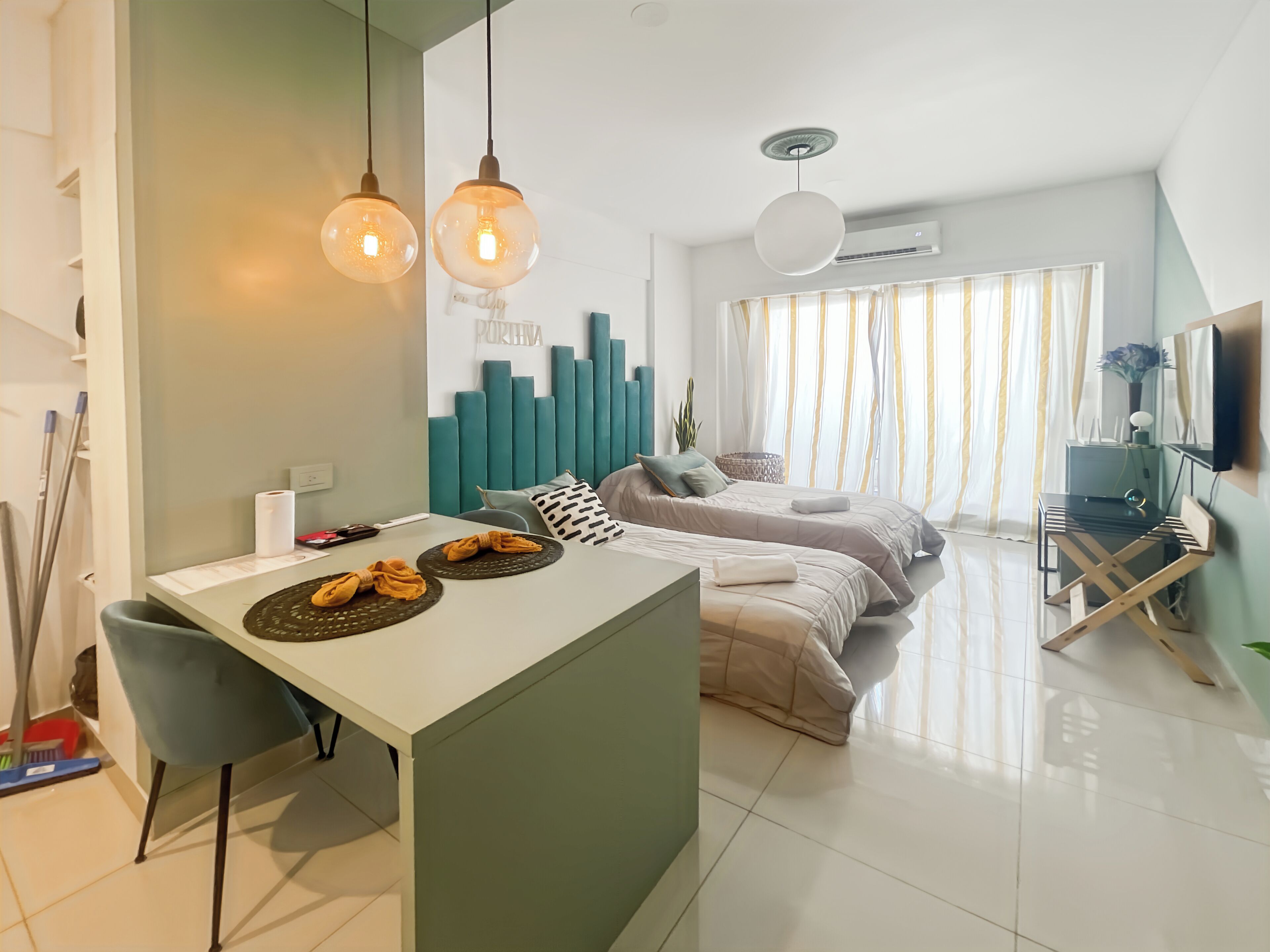 A modern hotel room with a central island, two beds, a dining area, and a TV.