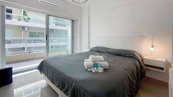 Habitación de hotel moderna con una cama grande, una mesita de noche con lámpara y vistas del exterior del edificio a través de la ventana.