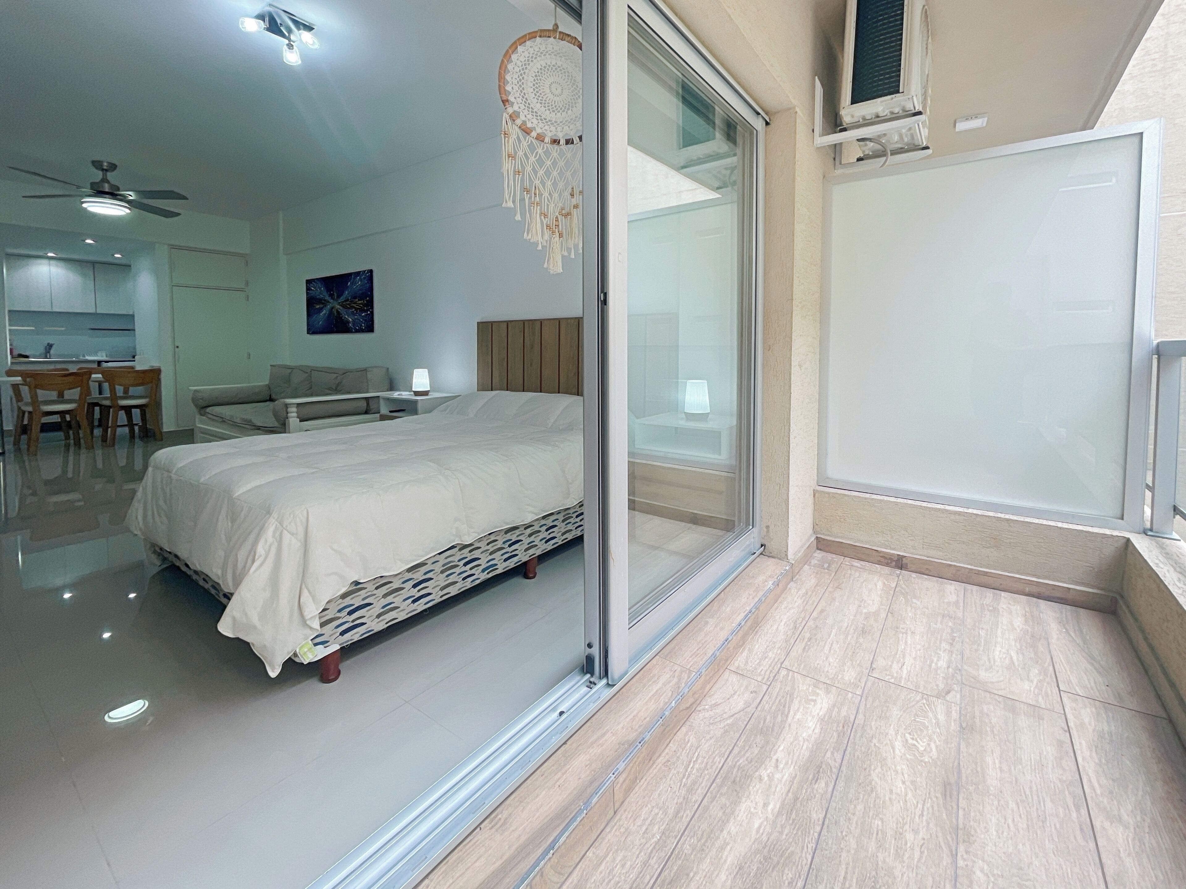A modern bedroom with a bed, a desk, and a chair. There is a sliding glass door leading to a balcony.