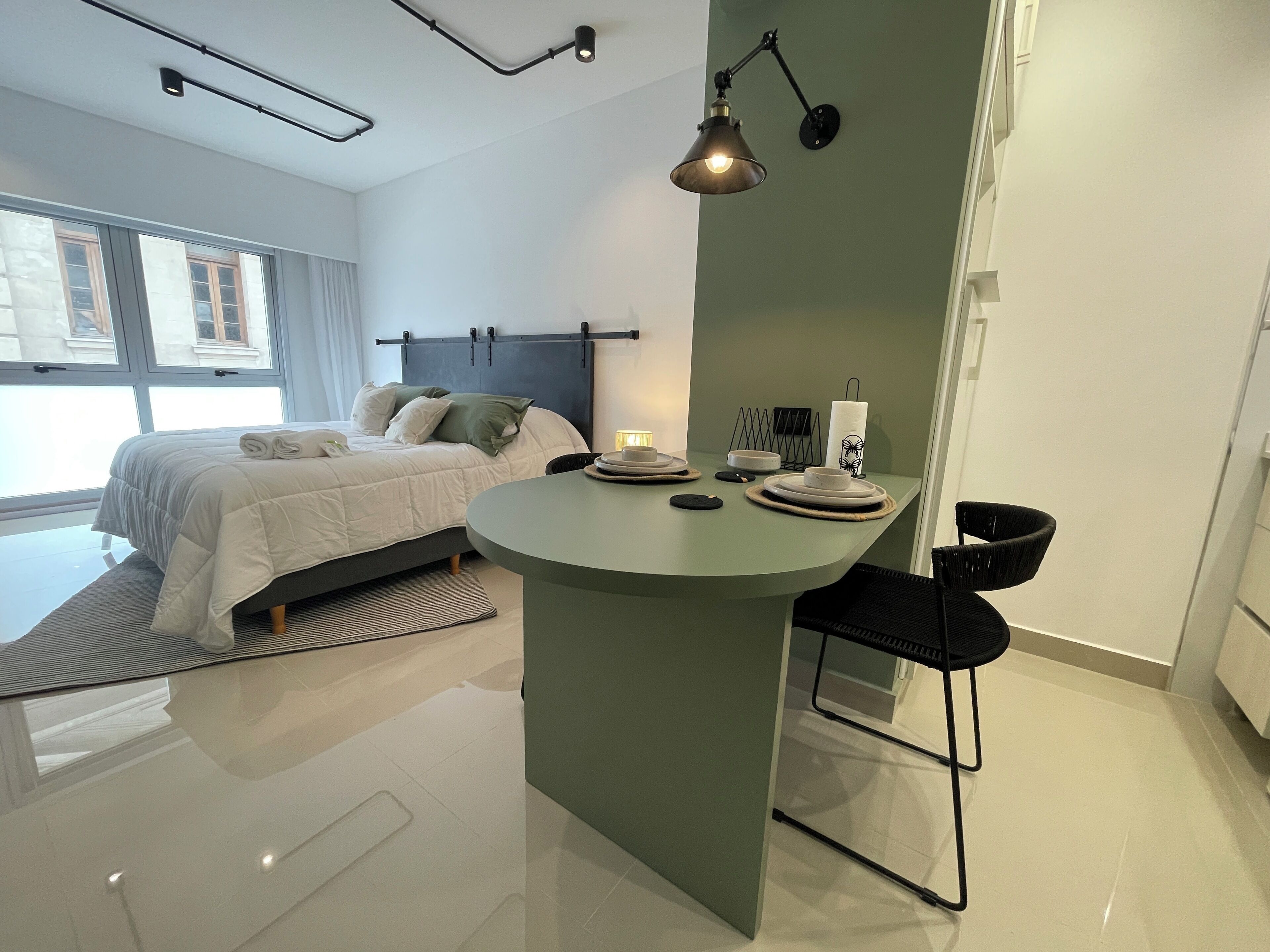 A modern bedroom with a bed, bedside table, and a small dining area with a table and chairs.