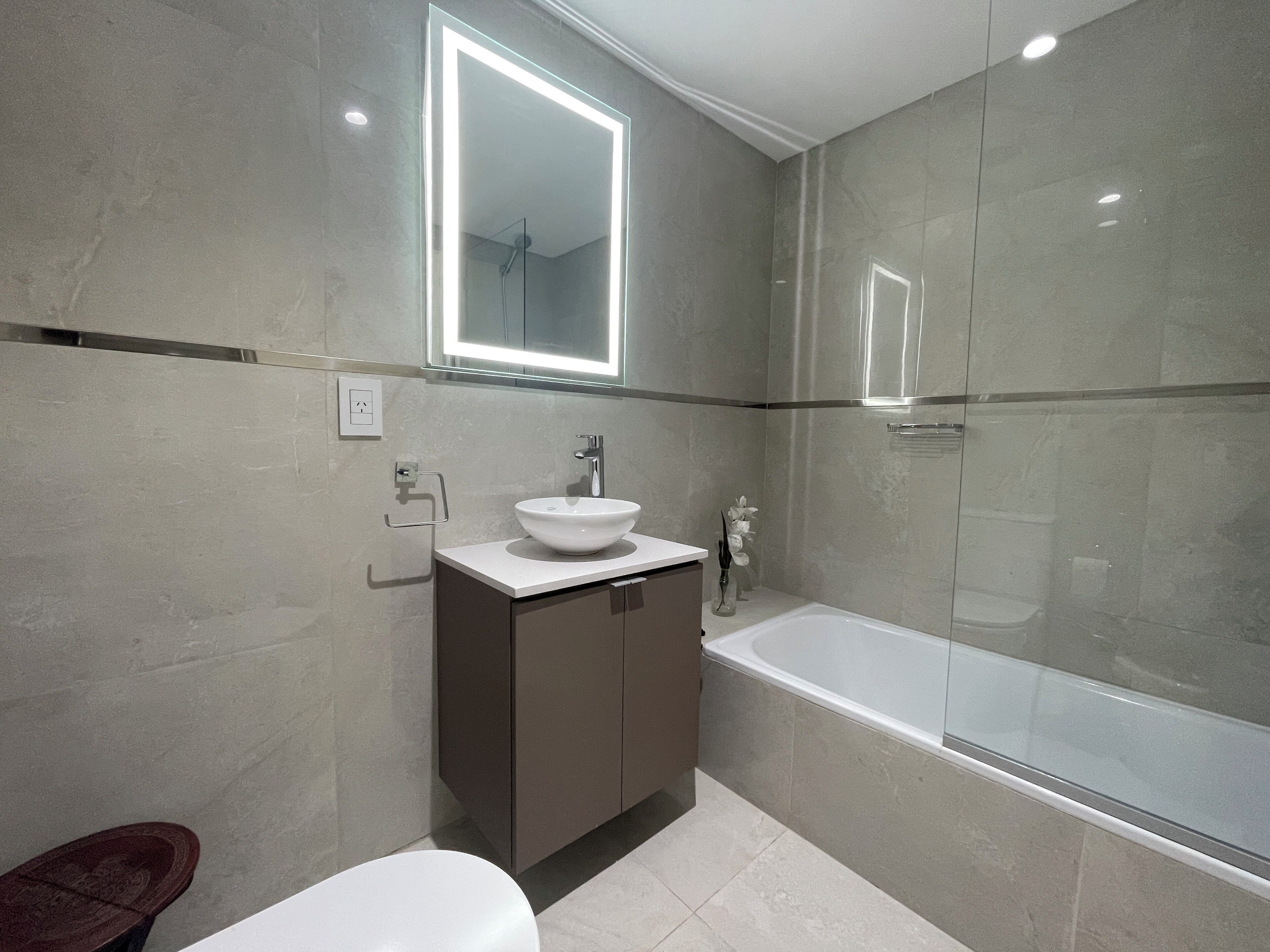 A modern bathroom with a glass-enclosed shower, a white sink, and a dark-toned cabinet.
