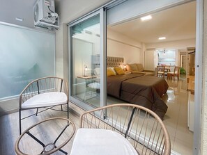 Een moderne slaapkamer met een groot bed, een glazen deur die uitkomt op een balkon, en een eethoek is zichtbaar door het glas.