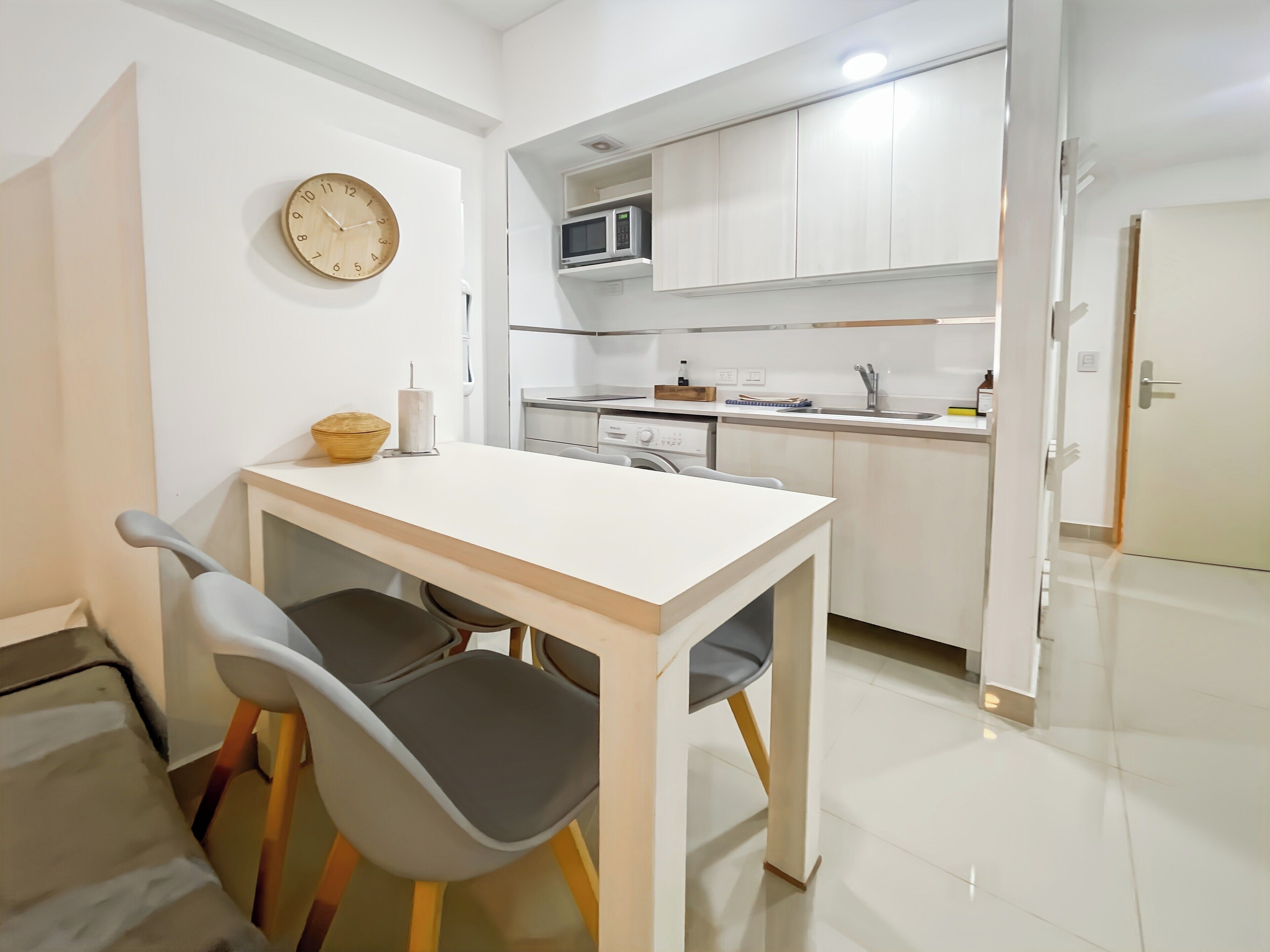 A modern kitchen with white cabinets, a microwave, and a sink. There is a dining table with two chairs.