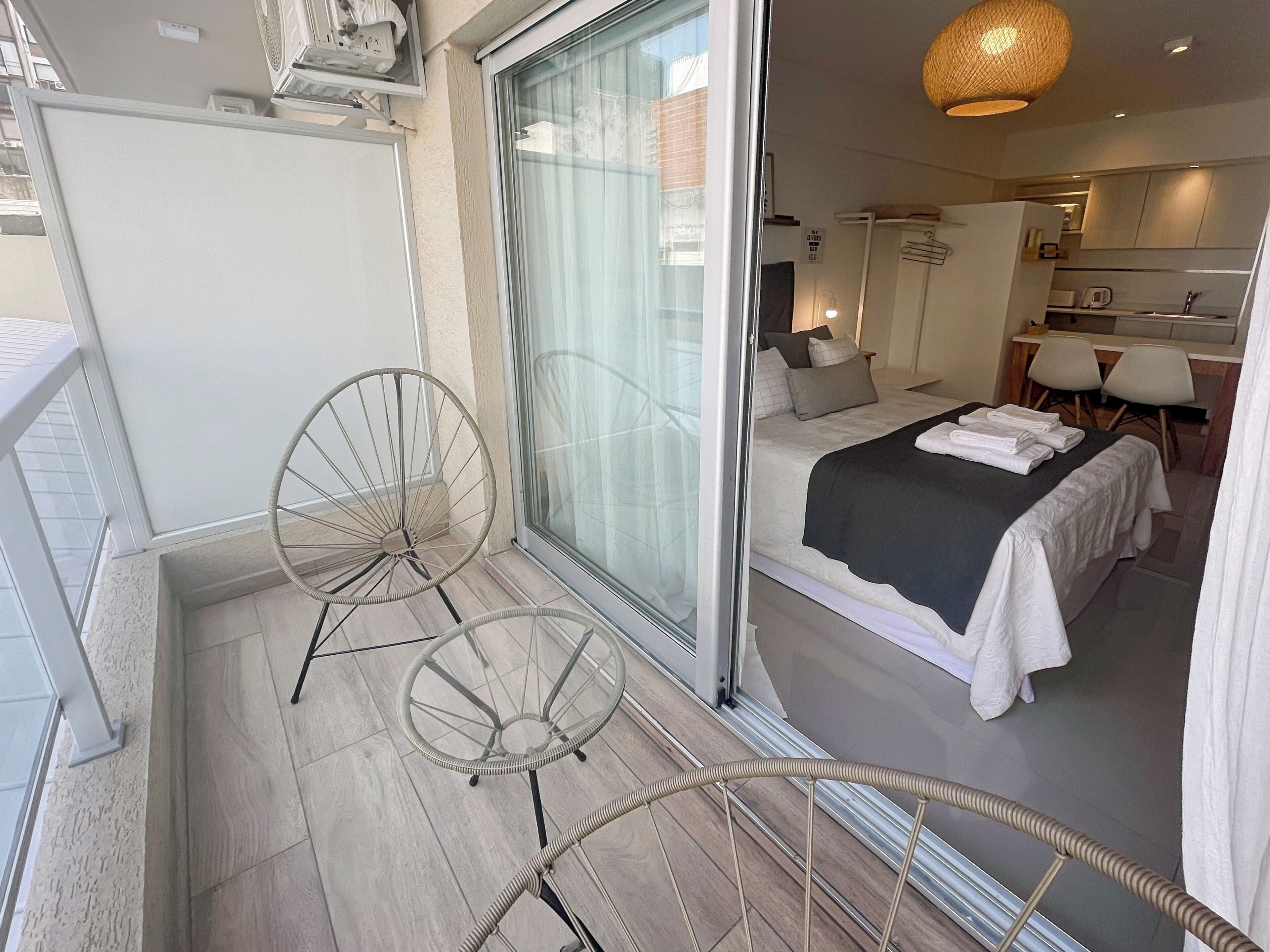 Ett modernt hotellrum med en balkong, en säng med vita sängkläder, ett litet köksutrymme och ett matbord.