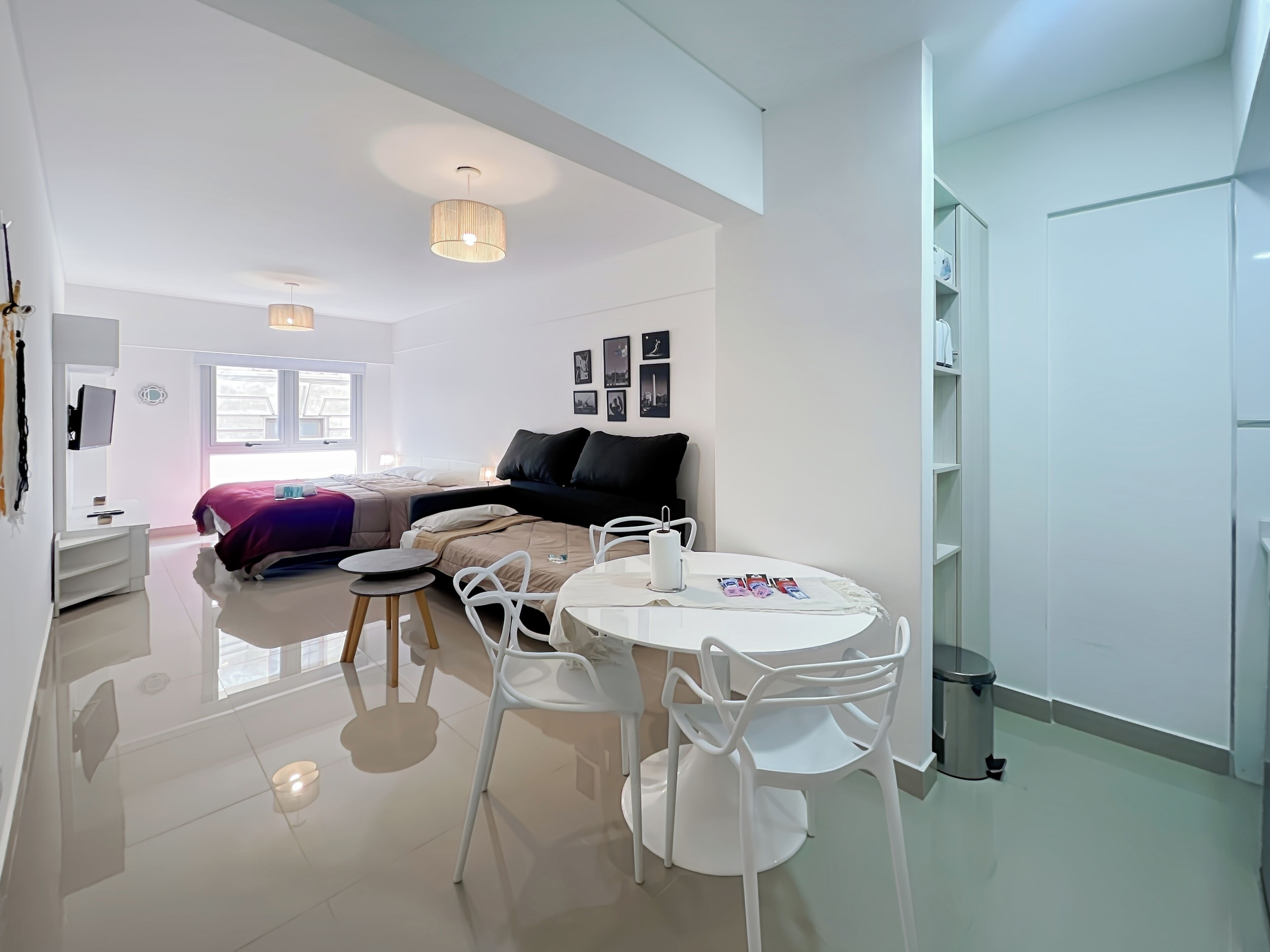 Een moderne, goed verlichte woonkamer met een eethoek, een bank en een aan de muur bevestigde televisie.