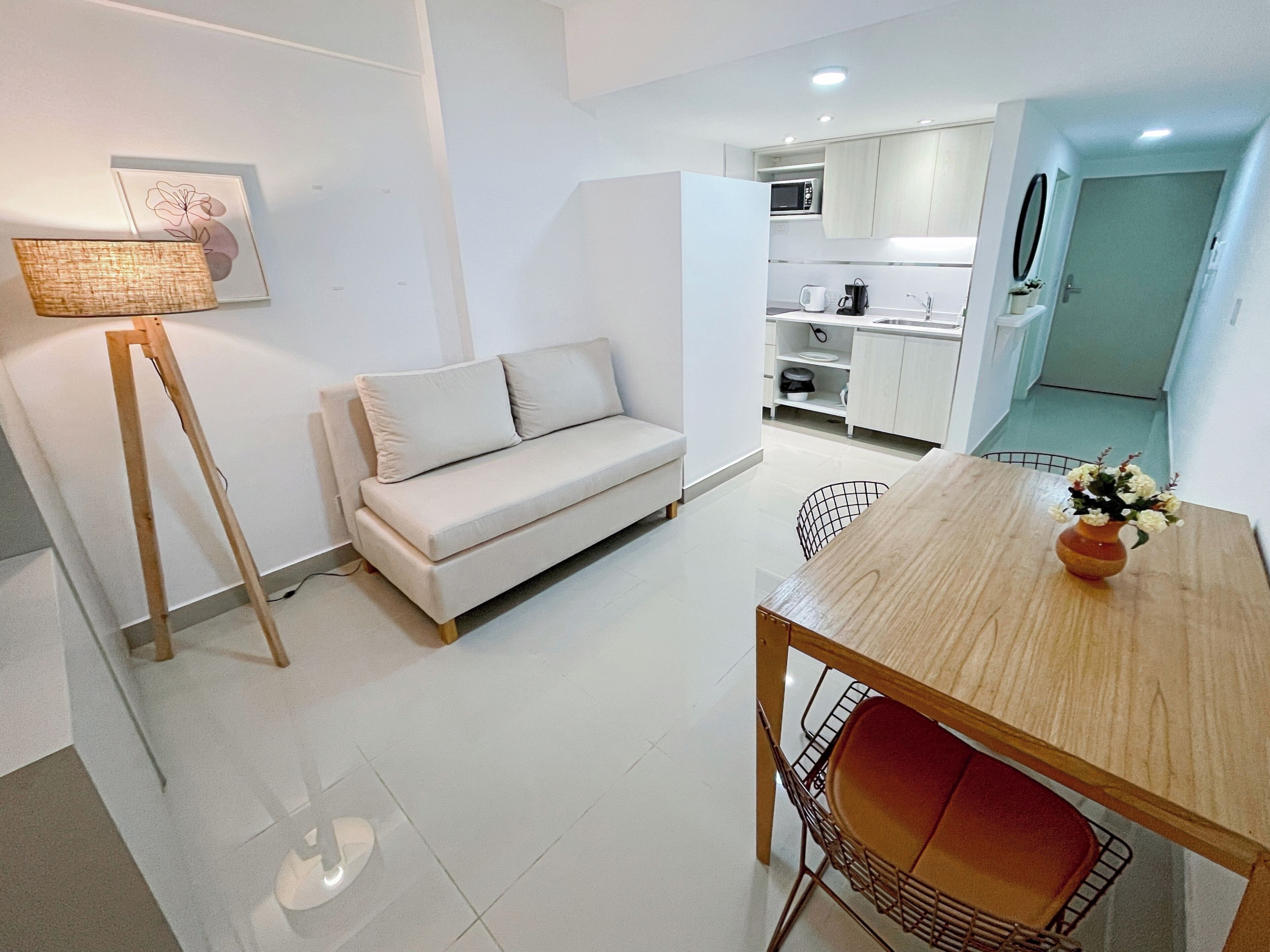 Un apartamento moderno con sala de estar que incluye un sofá, una mesa de comedor con sillas, una lámpara y una cocina al fondo.