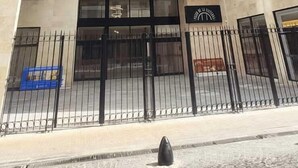Un edificio moderno con fachada de vidrio reflectante, varios pisos y una entrada protegida por un portón.