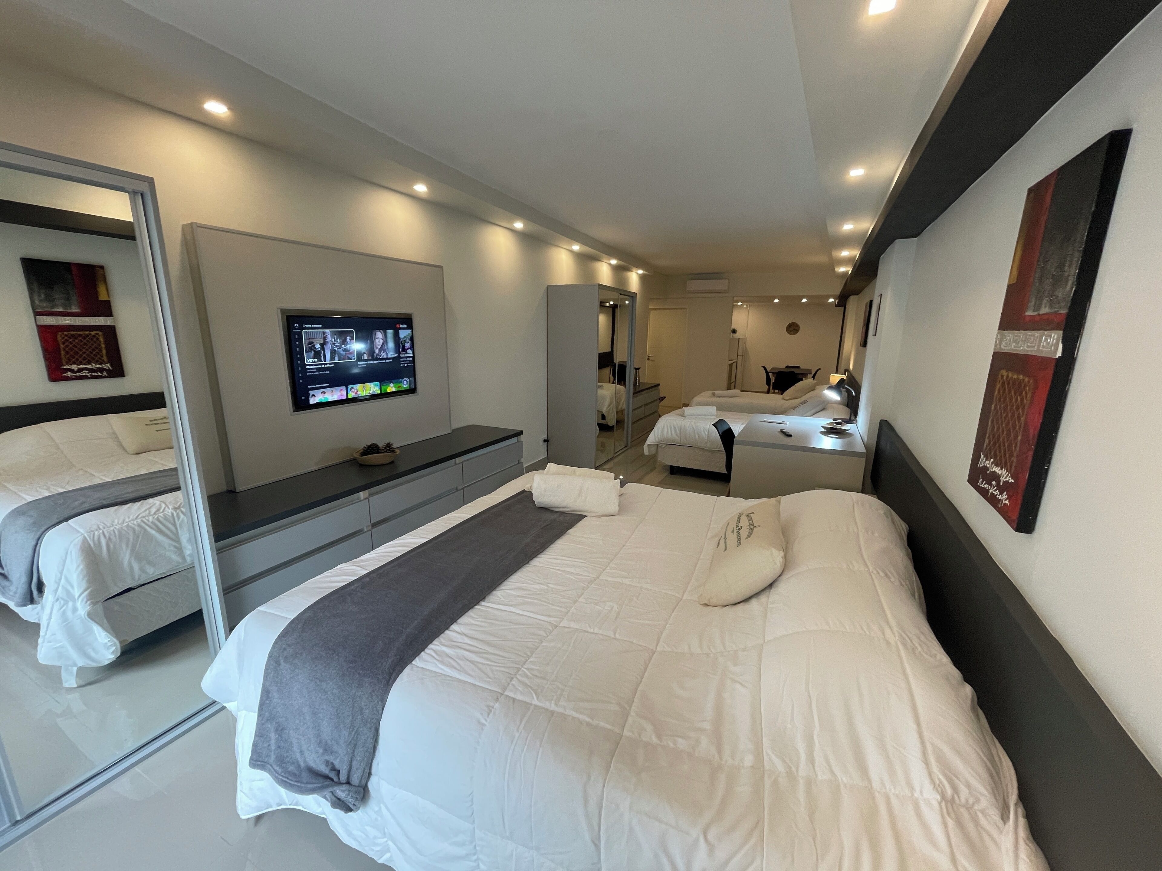 A modern hotel room with a large bed, a bedside table, a TV mounted on the wall, and a mirror.