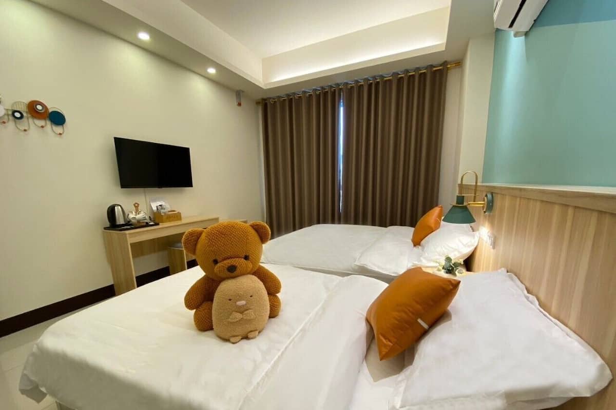 Une chambre d’hôtel avec deux lits, un téléviseur à écran plat, un bureau et un ours en peluche sur l’un des lits.