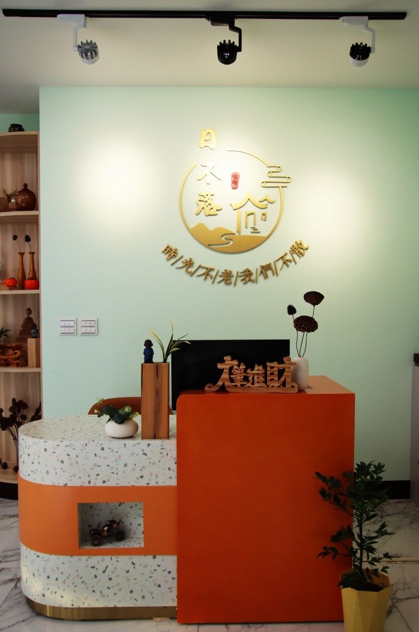 A reception desk with a logo and Chinese characters, a shelf with decorative items, and a potted plant.
