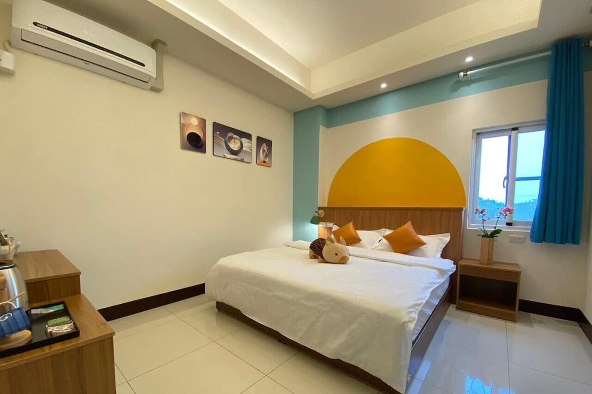 Une chambre d’hôtel équipée d’un lit, d’une table de chevet, d’un appareil de climatisation, d’œuvres d’art et d’une fenêtre avec des rideaux.