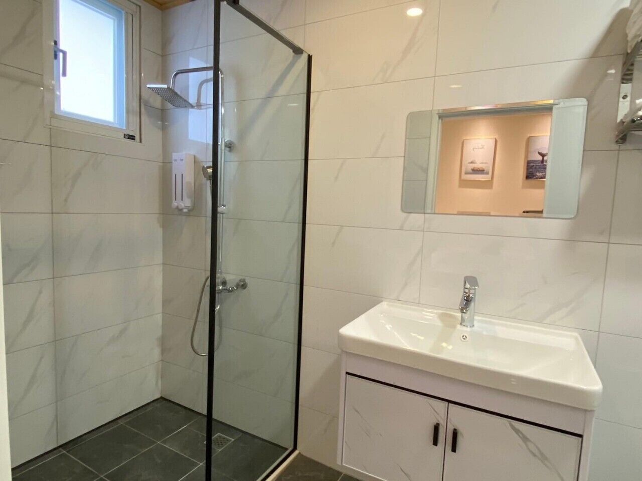 Un baño moderno con cabina de ducha de vidrio, un lavabo blanco y un espejo pequeño encima.