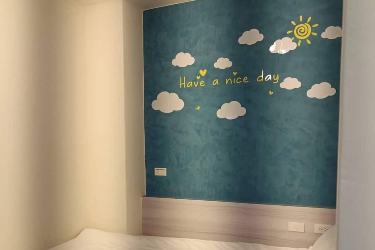 Une chambre à coucher comprenant un lit, un interrupteur fixé au mur et un mur décoratif orné d’un motif représentant un ciel et des nuages.