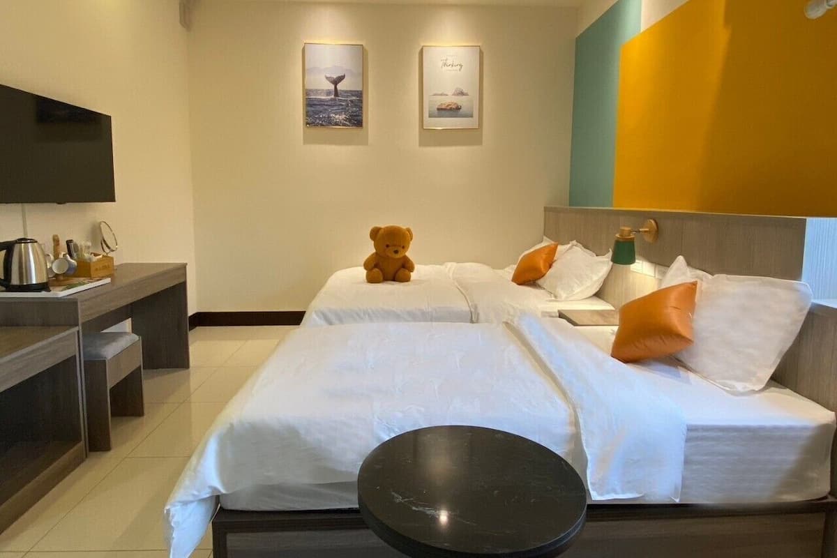 Une chambre d’hôtel avec deux lits, une table de chevet avec une bouilloire, une petite table ronde et deux tableaux encadrés au mur.