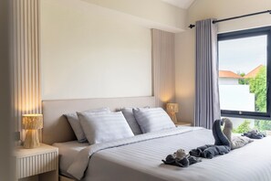 A modern hotel room with a large bed, two bedside lamps, and a view of greenery outside. - Jane Berawa Villa by Betterplace (Canggu)