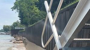A beach with a metal staircase leading down to the water, surrounded by a wooden fence.