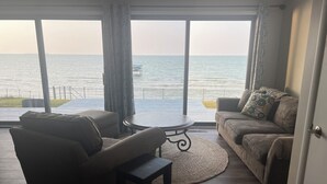 A living room with a view of the sea, a sofa, a coffee table, and a chair.