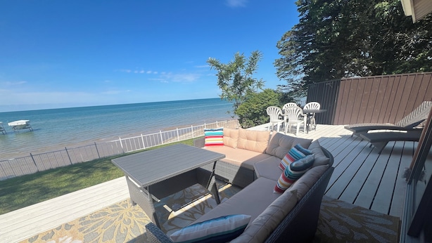 A deck with a sofa, chairs, and a table overlooking a beach.