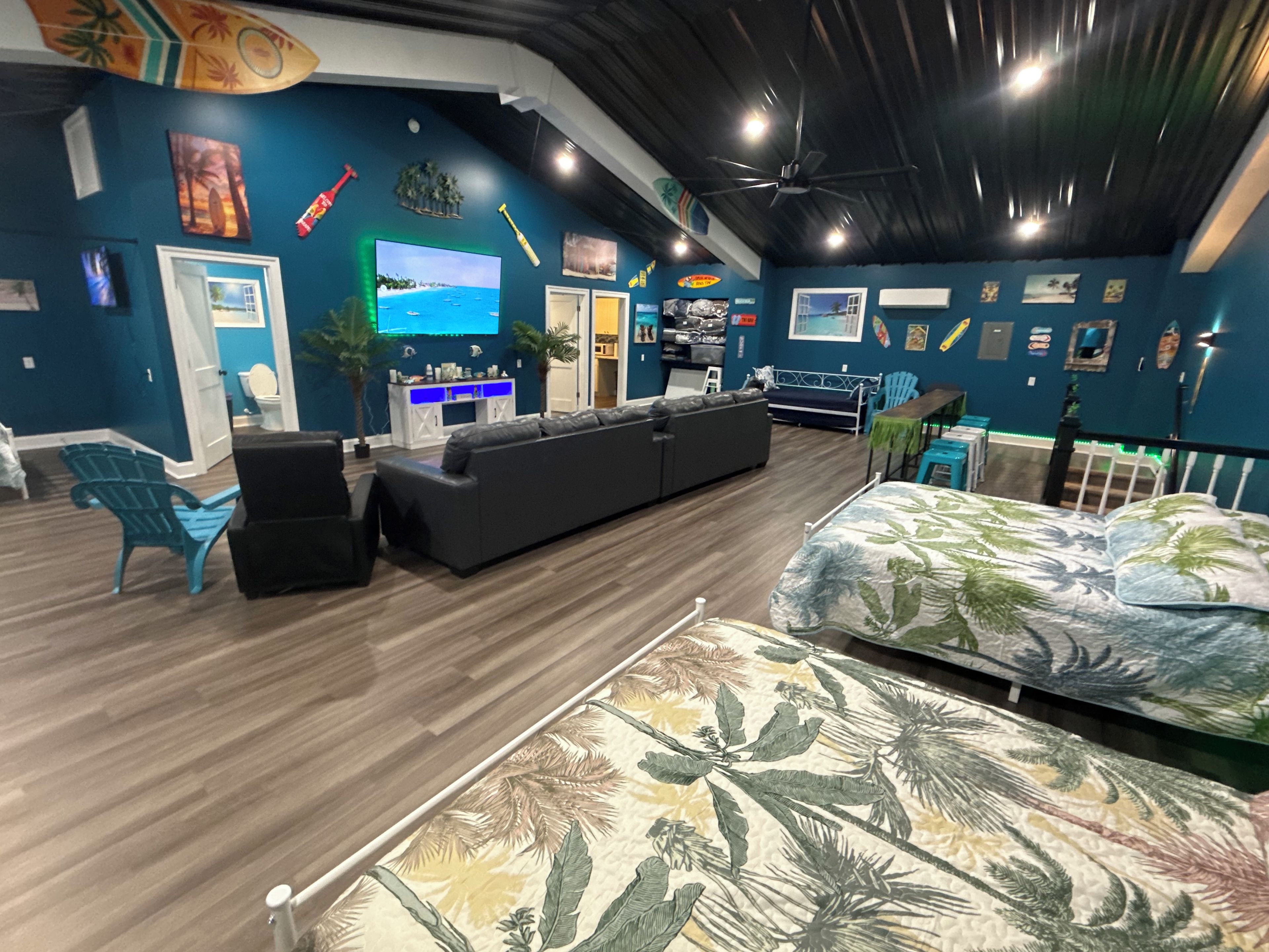 A room with a large bed, a sofa, a TV, and a ceiling fan.