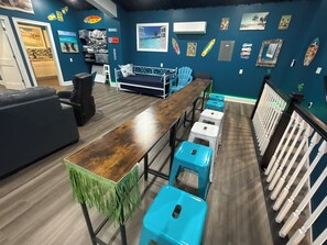 Um quarto com uma longa mesa de madeira, cadeiras azuis, um sofá e uma escada com balaústres brancos.