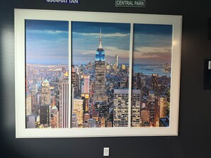 A framed cityscape artwork with a view of Manhattan's skyline, including the Empire State Building, mounted on a wall. - HUGE BEACH/TRAVEL THEME BARNDO (Elizabeth City)