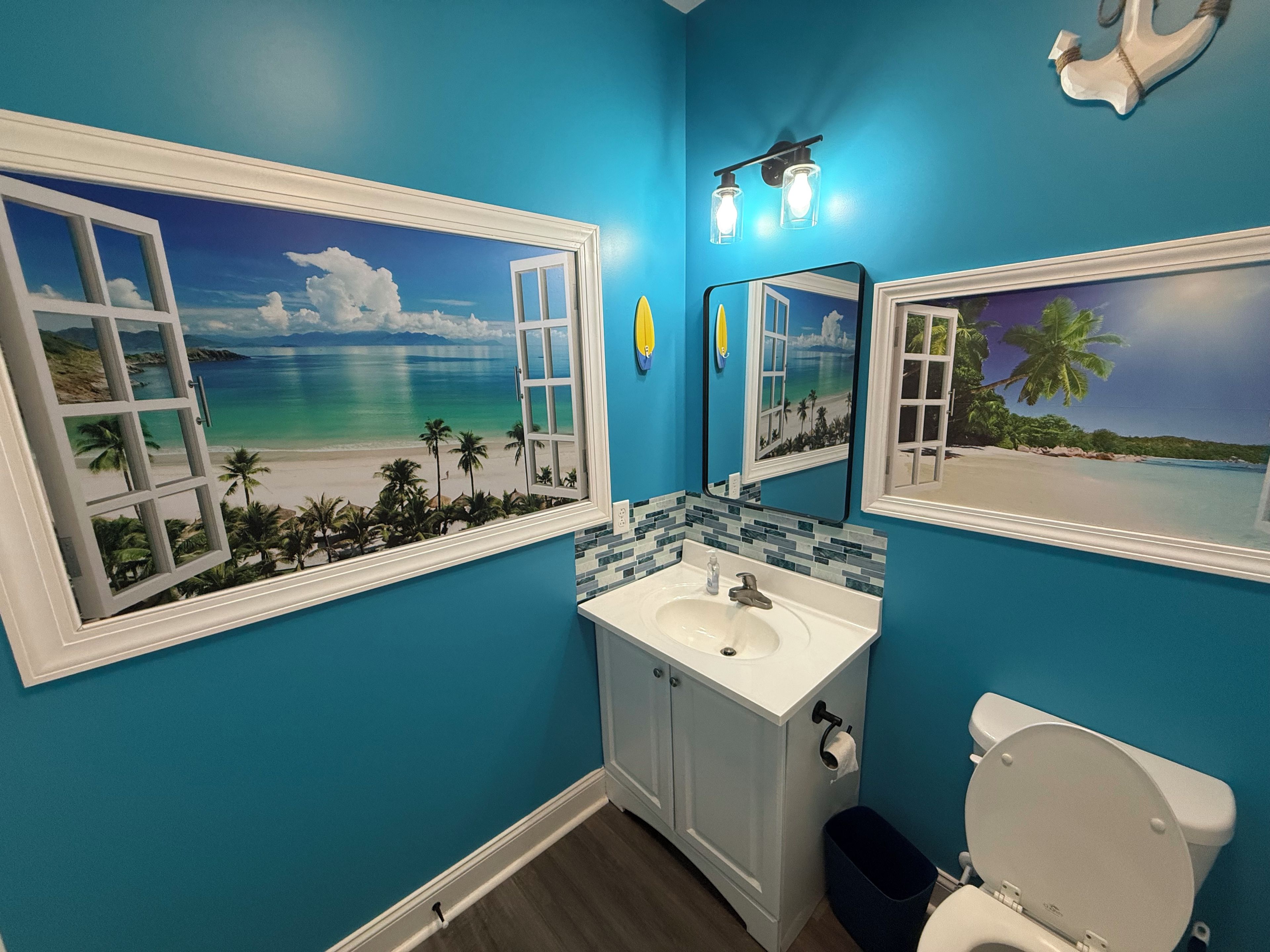 Une salle de bain avec une fresque murale sur le thème de la plage, un lavabo blanc et des toilettes.