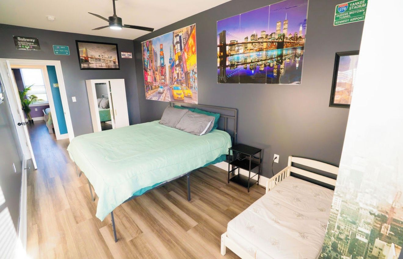 A bedroom with a bed, a nightstand, and a wall with cityscape posters.