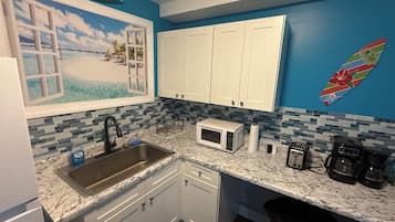 A kitchen with white cabinets, a sink, a microwave, and a coffee maker.