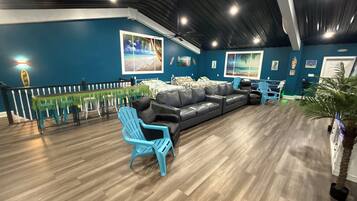 Una habitación con una pared azul oscuro, un sofá de cuero negro y una silla azul. Hay pisos de madera y un techo con vigas a la vista.