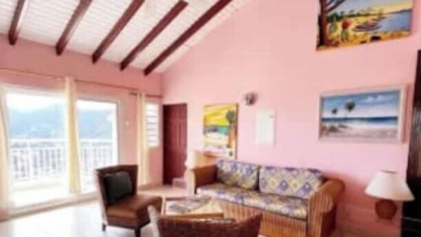 Amplia sala de estar con sofá, sillón y una mesa de centro. Hay un cuadro en la pared y una ventana que ofrece vistas.