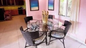 Un comedor con una mesa redonda y seis sillas, una cocina al fondo, y dos cuadros en la pared.