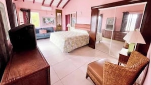 Un dormitorio con cama, televisión, una silla de mimbre y espejo.