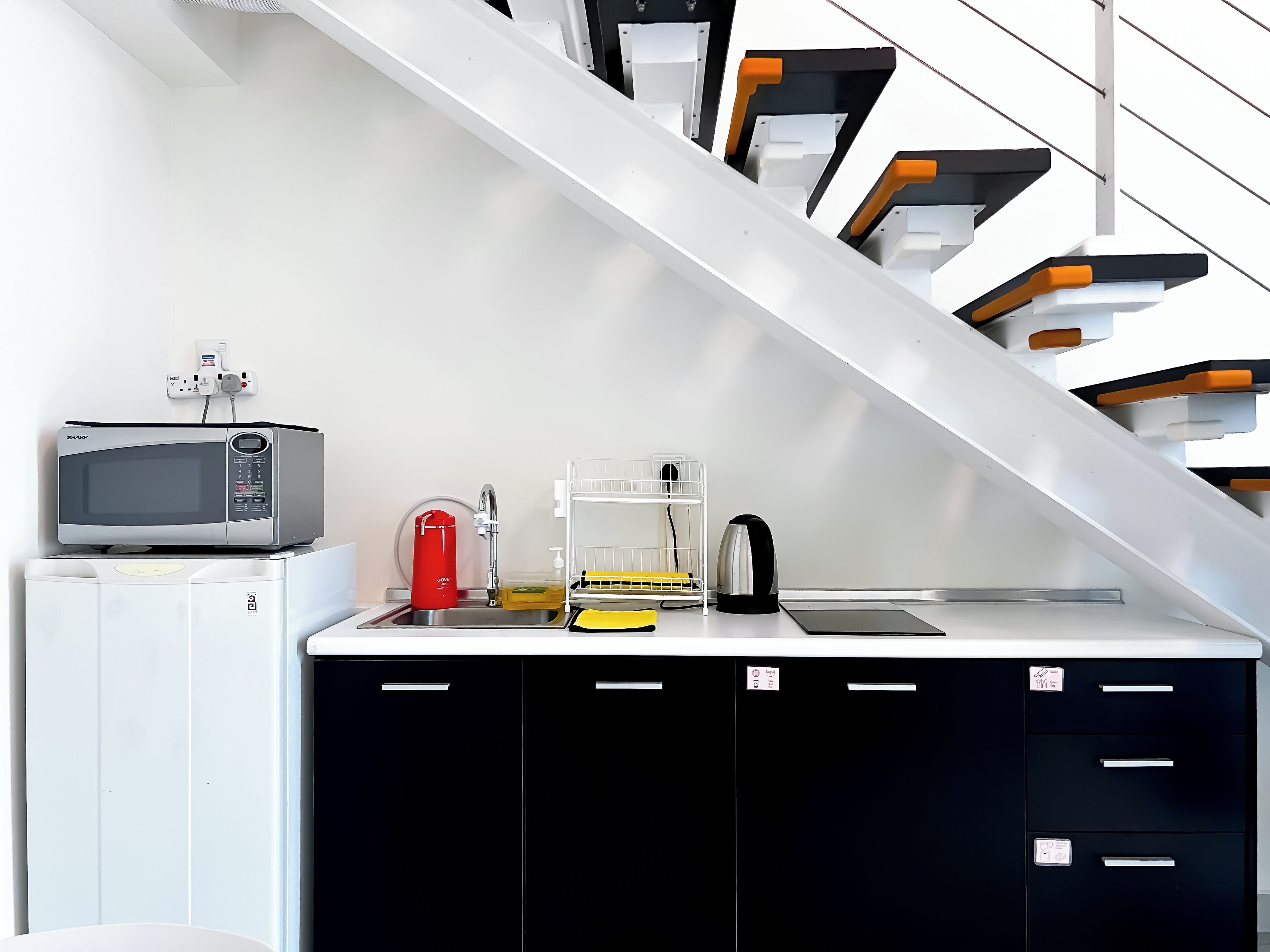 Una kitchenette compacta con microondas, tetera y lavabo.