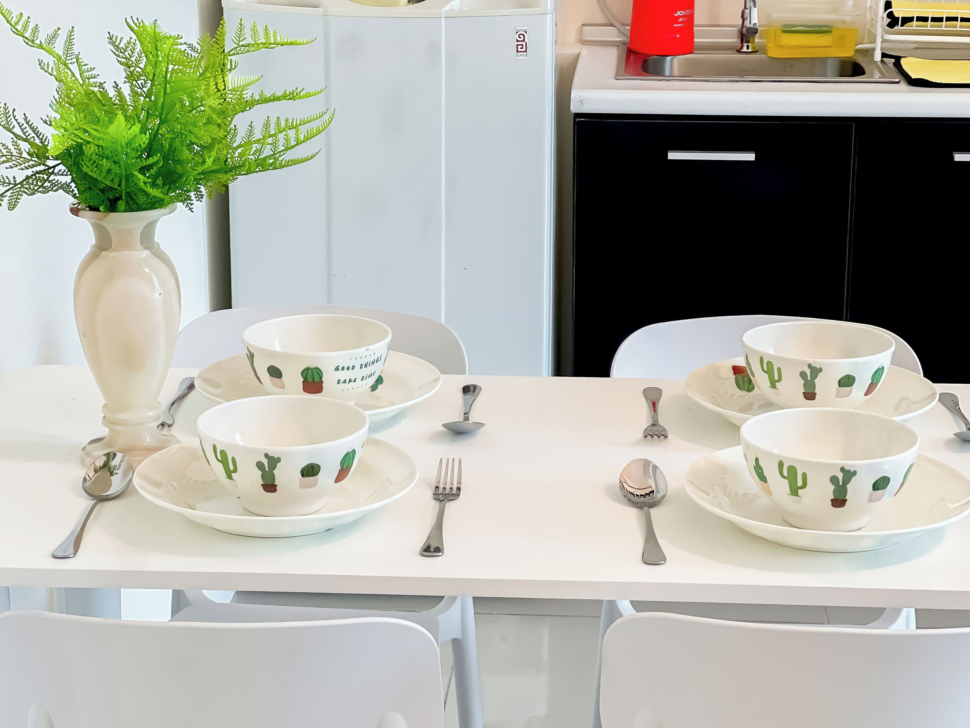 A dining table set with white plates and bowls featuring cactus designs, accompanied by silverware.