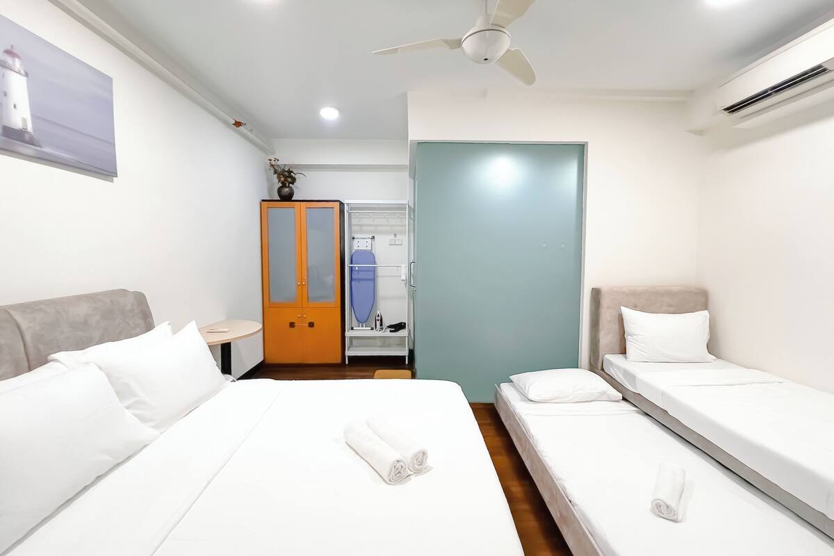 Una habitación de hotel con dos camas, un armario, un ventilador de techo y un baño con ducha e inodoro.