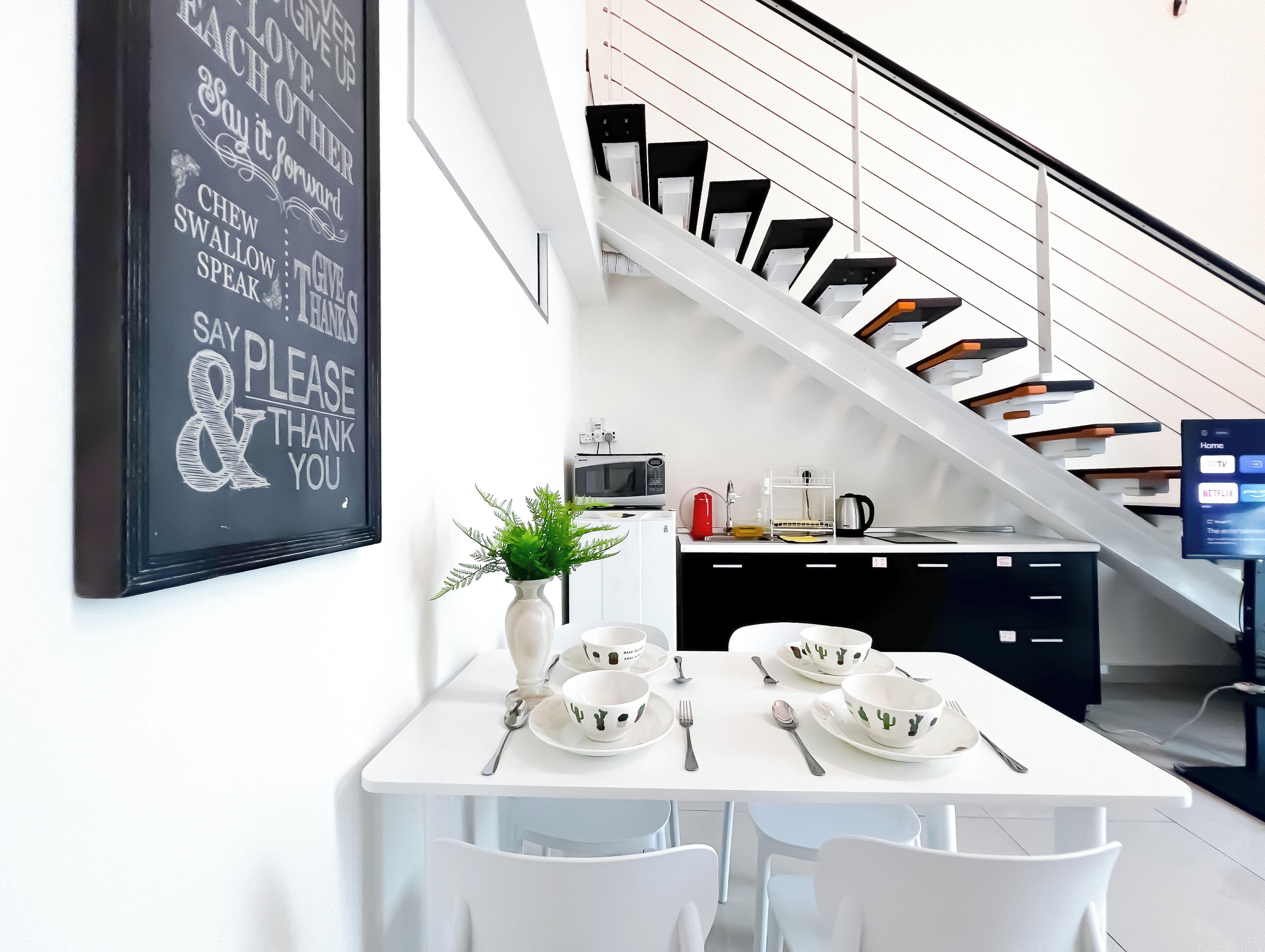 A modern kitchen with a dining area, white furniture, a staircase, and a motivational wall.