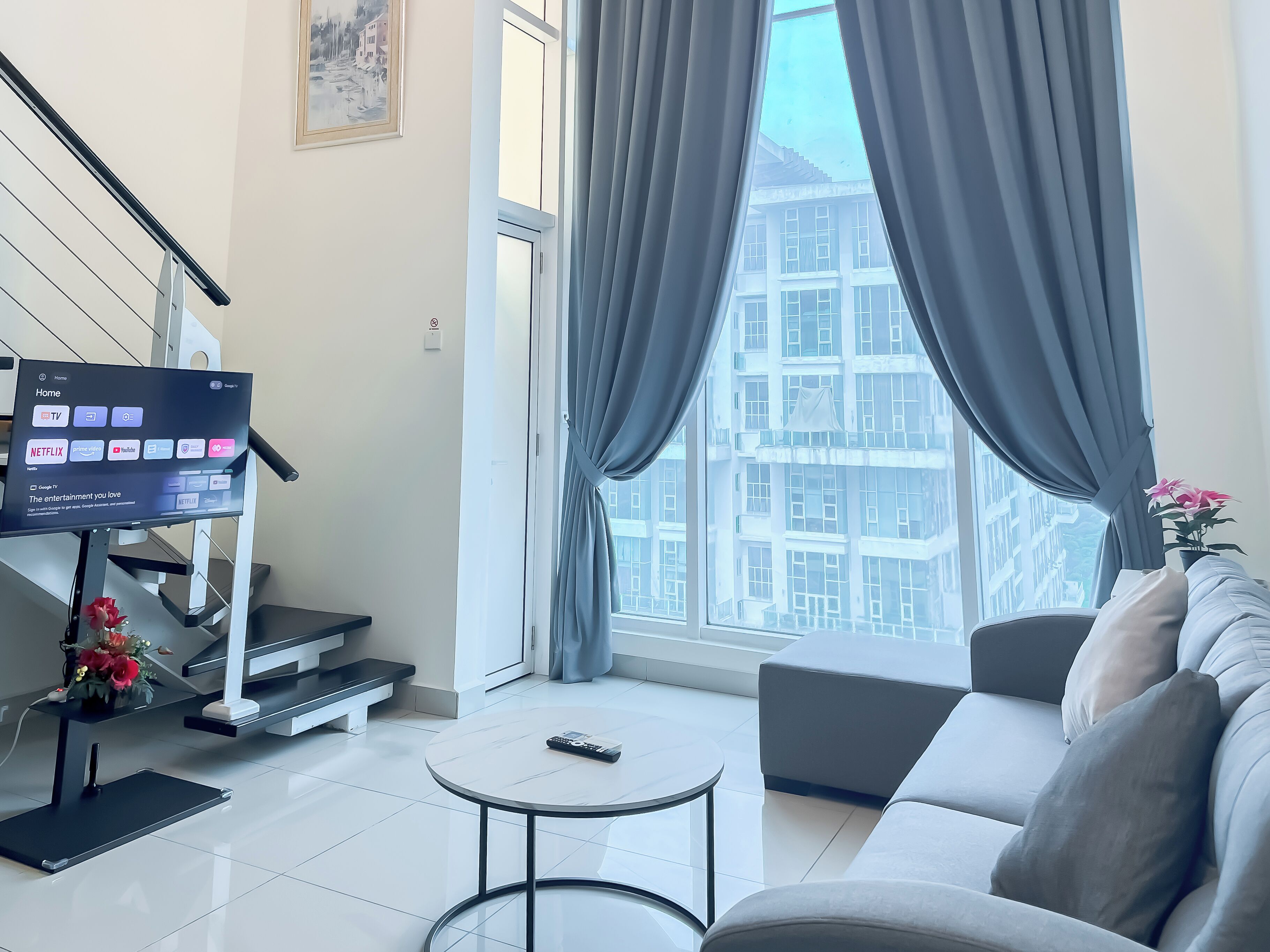 A modern living room with a flat-screen TV, a sofa, a coffee table, and a staircase.